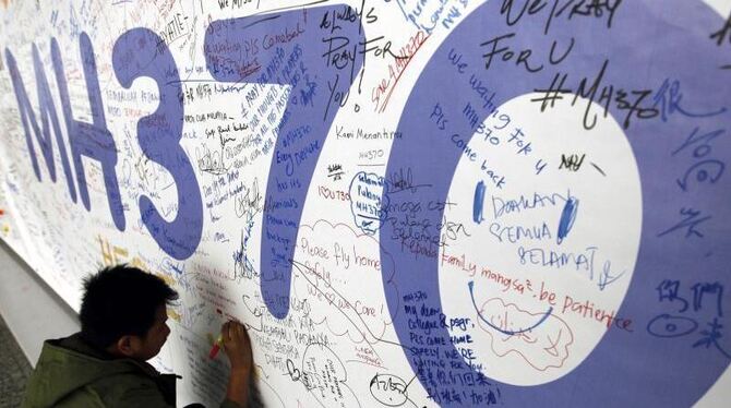 EinPMann schreibt 2014 eine Nachricht an Passagiere des verschwundenen Fluges auf ein Banner am Flughafen von Kuala Lumpur. F