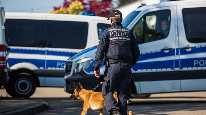 Einsatz in Rottenburg: Ein Polizist läuft mit einem Polizeihund an Polizeieinsatzfahrzeugen vorbei.
