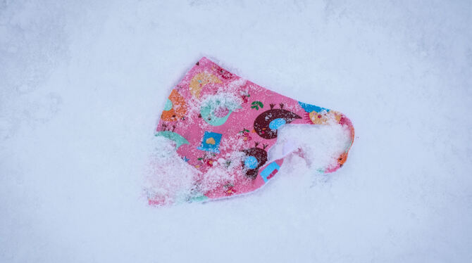 Ein verlorener, bunt gemusterter Mund-Nasen-Schutz für Kinder liegt im Schnee auf dem Gipfelplateau des Großen Feldbergs.