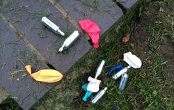 Weggeworfene Lachgas-Kartuschen und Luftballons liegen in einem Park.