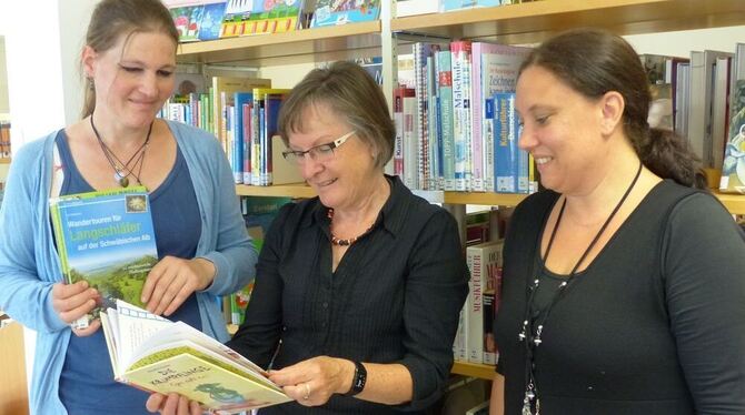 Bücherei-Leiterin  Charlotte Braun (Mitte) schaut in das Buch, das Carolin Knapp (links) fürs Vorlesen und für sich ausleihen mö