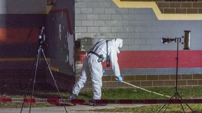 Ein Polizist untersucht in Weimar vor einem Haus Spuren auf einen Rasenstück. Foto: Johannes Krey