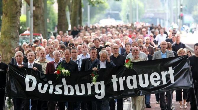 Teilnehmer eines Trauermarsches ziehen in Duisburg nach einem improvisierten Gottesdienst zur Unglücksstelle. 