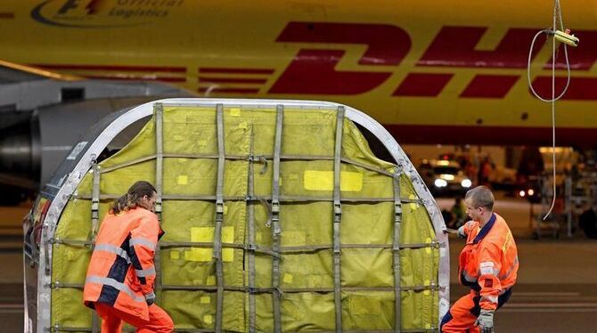 DHL-Mitarbeiter ziehen einen Luftfrachtcontainer zum Entladen ins DHL Hub auf dem Flughafen Leipzig/Halle (Archivbild).