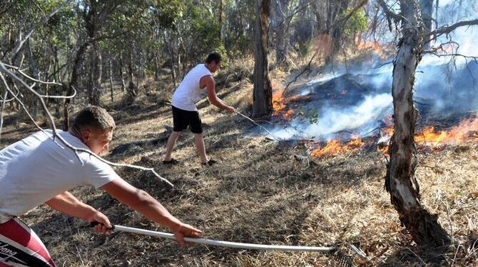 Zwei Australier versuchen die sich ausbreitenden Flammen zu stoppen.