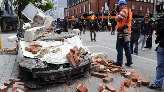 Reporter vor einem zerstörten Auto in der Innenstadt.