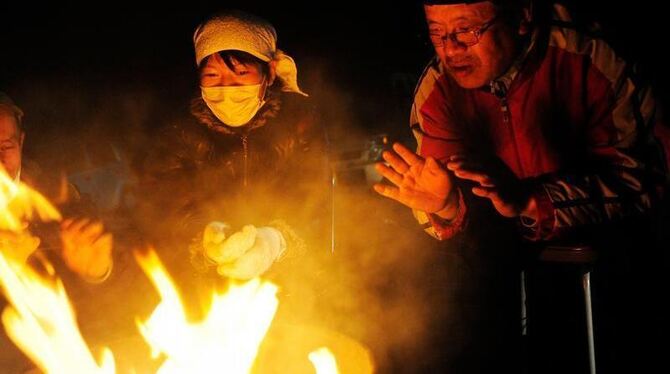 Bewohner der Stadt Rikuzentakata wärmen sich an einem Lagerfeuer.