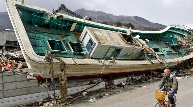 Nach dem Tsunami: Ein Fahrradfahrer passiert in Ofunato ein vom Tsunami in ein Haus geschleudertes Schiff.