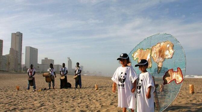 Kinder mit einem WWF-T-Shirt stehen am Strand von Durban vor einer stilisierten Erde. Mit einer symbolischen Übergabe einer v