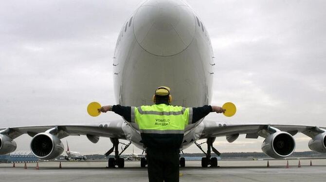 Ein Mitarbeiter der Vorfeldaufsicht weist ein Flugzeug zu seiner Parkposition ein. Foto: Frank May/Archiv