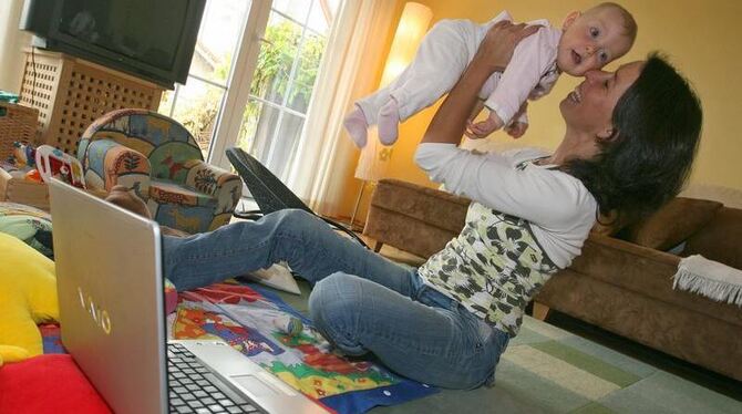 Betreuung zu Hause: Eine Hausfrau spielt, vor dem Laptop sitzend, mit ihrem Baby. Foto: Karl-Josef Hildenbrand/Archiv