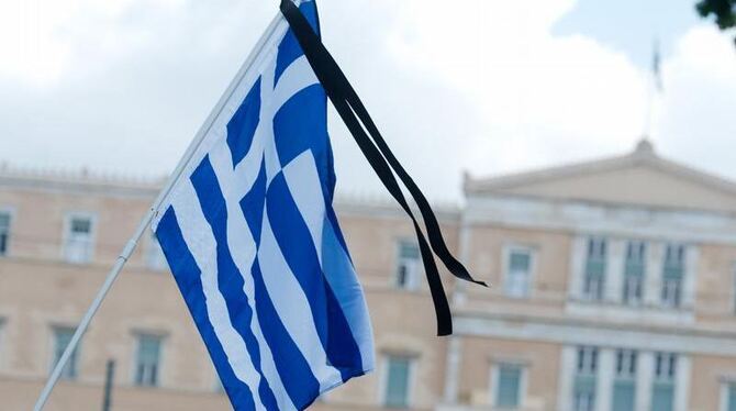 Demonstranten zeigen die griechische Flagge mit Trauerflor vor dem Parlament in Athen. Foto: Maurizio Gambarini/ Archiv