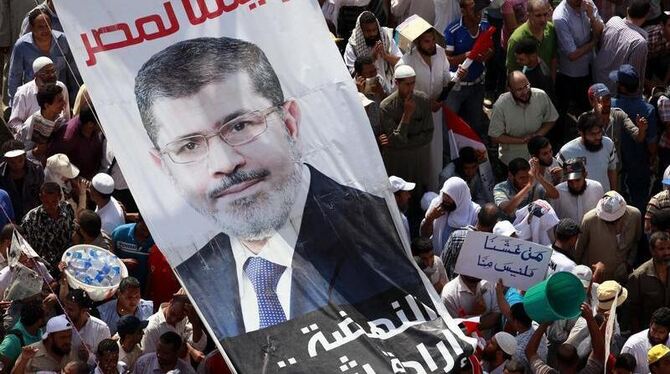 Ägyptische Demonstranten halten ein Plakat mit dem Konterfei von Mohammed Mursi. Ägyptens Präsident liegt im Clinch mit Milit