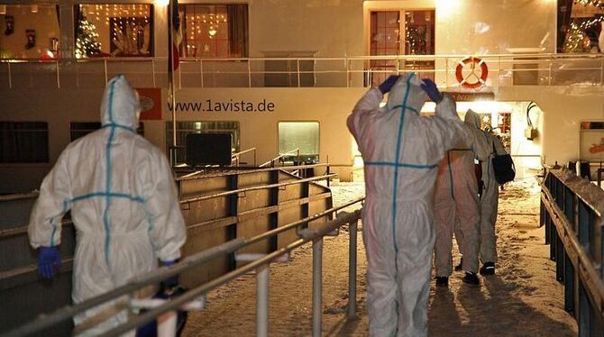 Rettungssanitäter in Schutzanzügen auf dem Weg zum Hotelschiff, auf dem viele Gäste an einer Infektion erkrankt sind. Foto: S