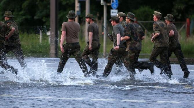 Bundeswehrsoldaten rennen im Ortsteil Rothensee in Magdeburg über eine überflutete Straße. Foto: Jens Büttner