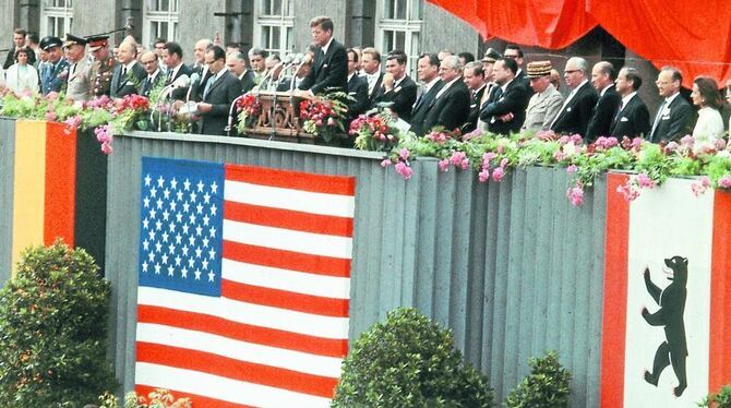 John F. Kennedy spricht auf dem Balkon des Schöneberger Rathauses, das mit deutschen und amerikanischen Flaggen dekoriert ist. F