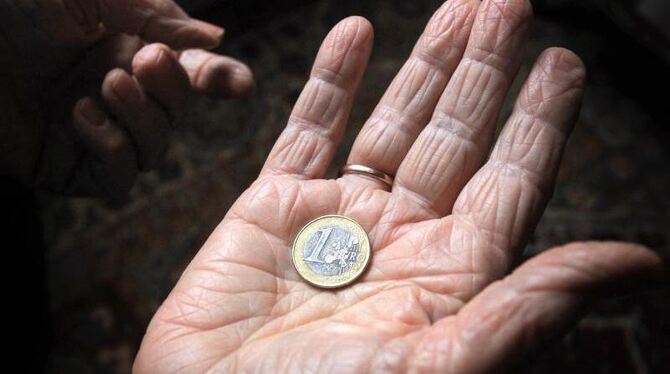 Wie den letzten Groschen hält eine ältere Frau eine Euromünze in der Hand. Foto: Karl-Josef Hildenbrand