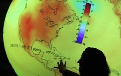 Eine Frau erklärt an einer beleuchteten Weltkugel den Klimawandel