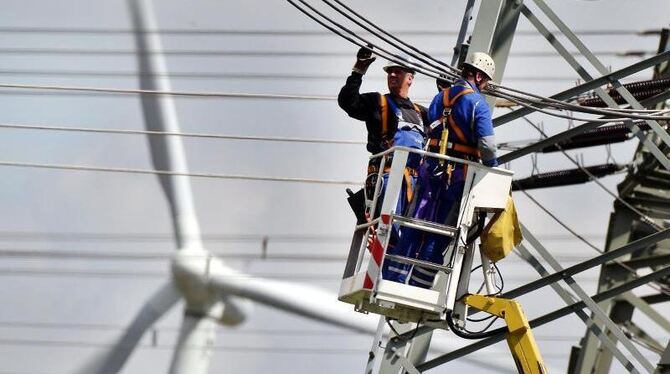 Arbeiter des Energieversorgers RWE arbeiten an Stromleitungen im Hochspannungsnetz, während sich im Hintergrund ein Windrad dreh