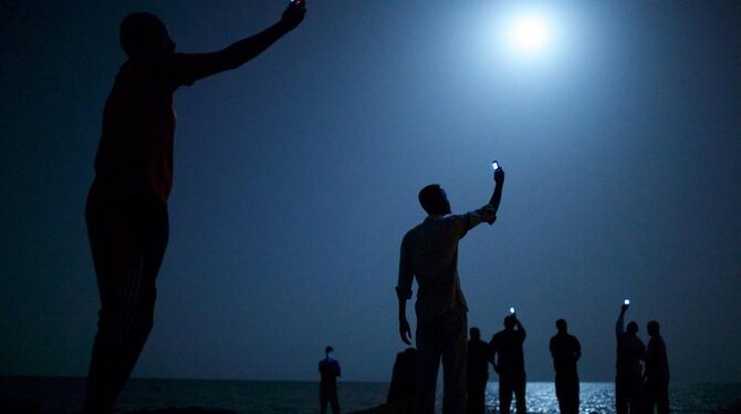 Das World Press Photo 2013 zeigt eine Gruppe afrikanischer Migranten an der Küste Dschibutis in der Nacht. Sie halten ihre Handy