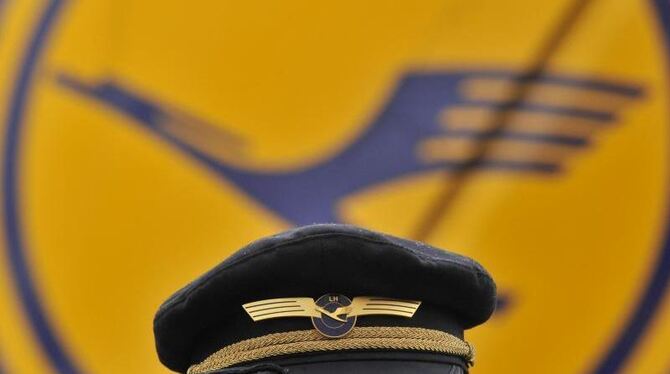 Ein Pilot der Lufthansa steht am Flughafen in Frankfurt am Main vor dem Lufthansa-Logo. Foto: Boris Roessler/Symbol