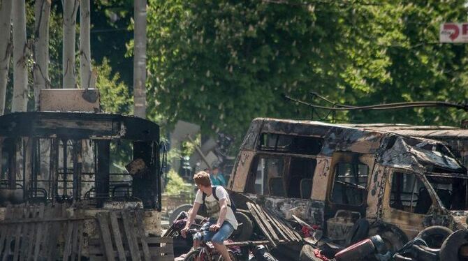 Ein Fahrradfahrer passiert ausgebrannte Buswracks im ostukrainischen Kramatorsk. Foto: Roman Pilipey