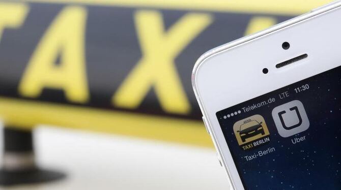 Die Handy-Apps »Uber« und »Taxi Berlin« sind auf einem Smartphone vor einem Taxi in Berlin. Foto: Jörg Carstensen/Symbol