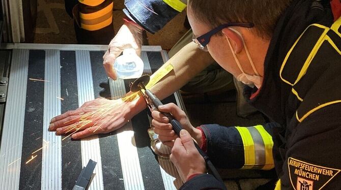 Ein Mann (Gesicht verdeckt) wird in München von der Feuerwehr und der Polizei mit einer Flex von einer Handschelle befreit.