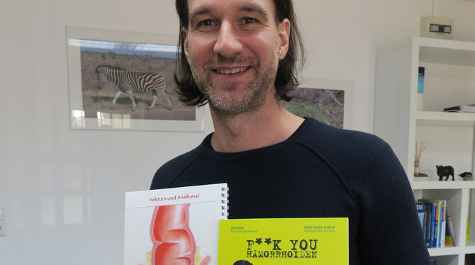 Derek Zieker-Fischer in seiner Proktologie-Praxis mit seinem Buch »F**ck You Hämorrhoiden« und einem Schaubild des Enddarms mit Derek Zieker-Fischer in seiner Proktologie-Praxis mit seinem Buch »F**ck You Hämorrhoiden« und einem Schaubild des Enddarms mit