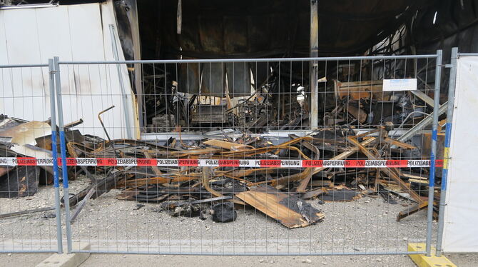 In der ausgebrannten Lagerhalle stehen verkohlte Lastwagen und Baumaschinen. Die Polizei hat den Brandort abgesperrt.