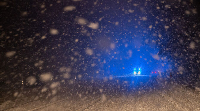 Im dichten Schneetreiben fährt ein Wagen mit Blaulicht auf einer schneebedeckten Straße.