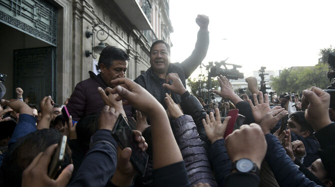 Der bolivianische Präsident Luis Arce erhebt eine geballte Faust, umgeben von Anhängern und Medienvertretern, vor dem Regierung