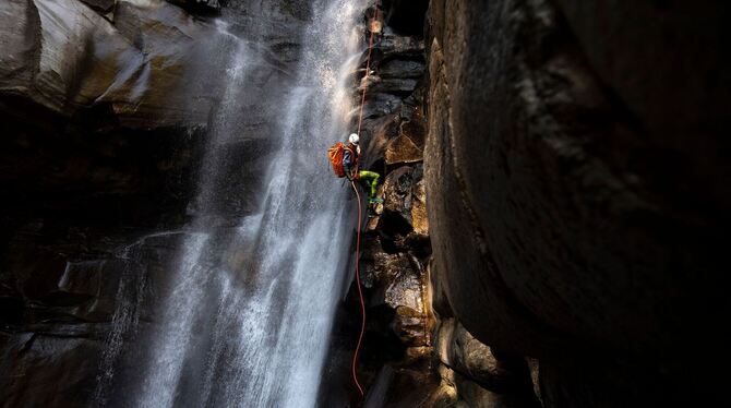 Ein Canyoning-Sportler klettert einen Wasserfall hoch.
