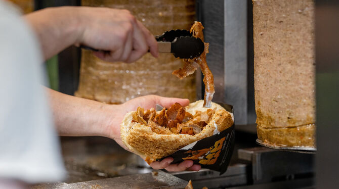 Ein Mitarbeiter einer Dönerbude legt Fleisch in einen Döner.