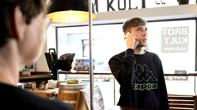 Ein junger Mann am Handy beim Besuch einer Bäckerei mit Café in Reutlingen. Wie fühlen sich die Angestellten, wenn Kunden smartp