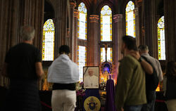 Menschen stehen am Ostermontag neben einem Foto des am Morgen mit 88 Jahren verstorbenen Papst Franziskus in der katholischen Ki