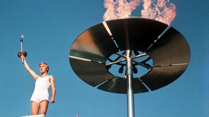 Der Schlussläufer der Fackelstafette, Günter Zahn, grüßt die im Stadion aufmarschierten Sportler, nachdem er das Olympische Feue