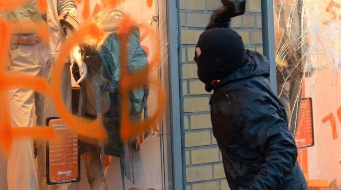 Ein Teilnehmer der Blockupy-Proteste wirft die Schaufensterscheibe eines Geschäfts ein. Foto: Arne Dedert