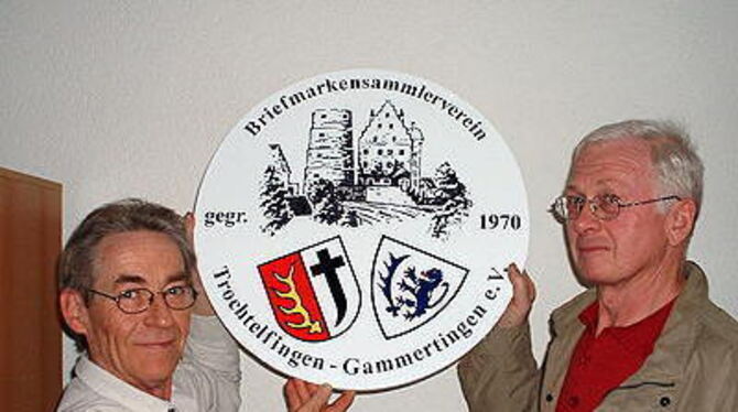 Vorbereitungen für ein großes Ereignis: Ekkehard Zerrull (links), Vorsitzender des Briefmarkensammlervereins Trochtelfingen-Gammertingen und Schriftführer Karl Eichkorn halten das Vereinswappen hoch, das auch die Medaillen des Wettbewerbs zieren wird. FOTO: HÄS