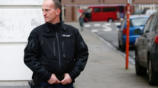 Ein Polizist sichert eine Straße in Brüssel, während im Hintergrund ein verdächtiger roter Van untersucht wird.