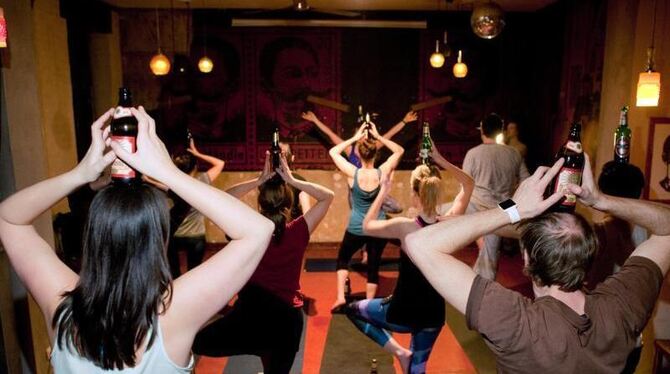 Teinehmer eines Bieryoga-Kurses vollziehen in Berlin in einer Kneipe eine Yogaübung mit Bierflasche. Foto: Klaus-Dietmar Gabb